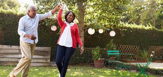 Senior black couple dance in their back garden, full length