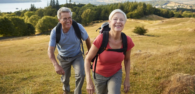 Portrait Of Senior Couple Climbing Hill On Hike Through Countryside In Lake District UK Together